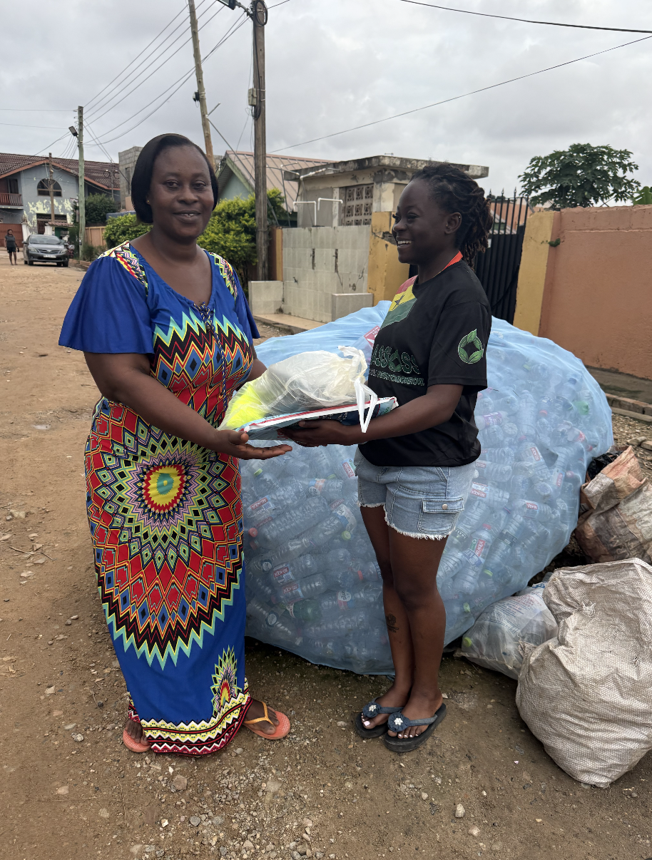 Plastoss team member handing PPE to a community member beside collected bottles